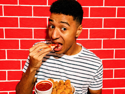 A young man enjoys crispy spicy chicken while reacting to the intense heat and bold flavours of the meal