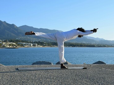 A practitioner in Warrior III overlooking the coastline, symbolising unwavering focus and inner strength