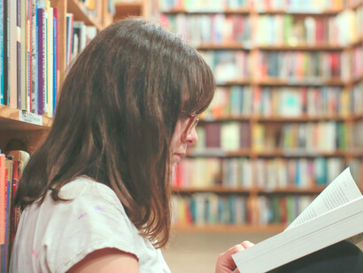 Estudiante se sienta en medio de los estantes de la biblioteca a leer