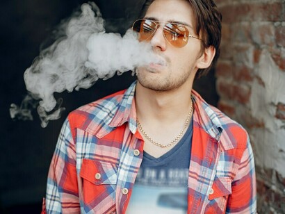 A man vaping in an urban setting, wearing a red shirt