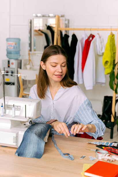 A designer working in a fashion studio, using a sewing machine and cutting fabric guided by zero-waste sewing patterns