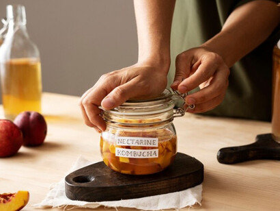A woman prepares a jar of nectarine kombucha, attaching a label to it