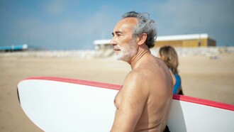 Idoso se prepara para surfar no mar. Lidar com as mudanças não é fácil. No entanto, ao equilibrar os sentimentos de perdas com fatores positivos, o idoso pode permanecer saudável e continuar a se reinventar ao passar pelas idades marcantes de 60, 70, 80 anos e além
