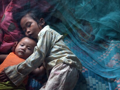Dos niños asiáticos en una cama junto a un mosquitero