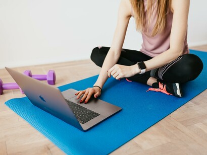 A woman sat on a yoga mat using a laptop 