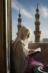 A woman in Egypt practices her worship rituals inside her home during Ramadan, with the two prominent minarets in the distance belonging to the Al-Rifa'i Mosque in Cairo, Egypt. Courtesy of @mustafa_shorbaji
