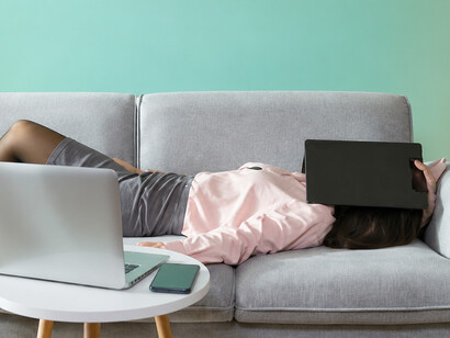 Asian professional lying on a couch, lost in thought as she reflects on technology and information overload