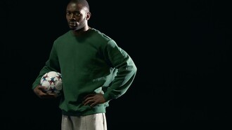 A man in a green sweater holding a soccer ball
