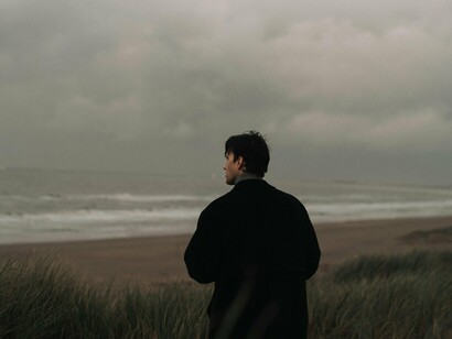 A man wrapped in darkness against an empty coast, reflecting the emotional distance that can grow within relationships