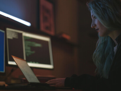 A programmer engaged with digital systems in a darkened workspace, reflecting the growing role of AI-assisted production