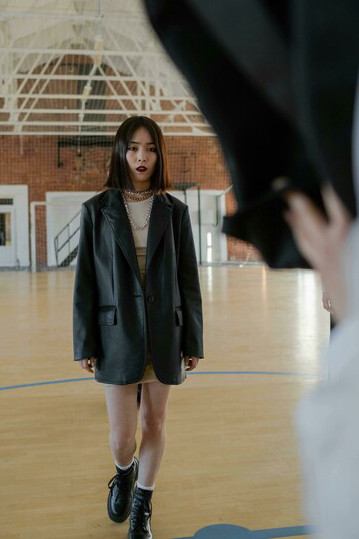 Young girl in an oversized black leather jacket stands on the basketball court as classmates grab her backpack, bullying her