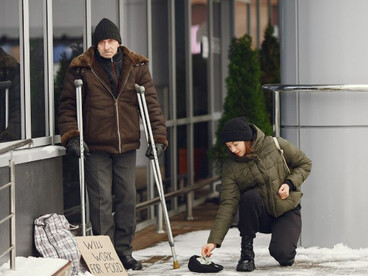 A homeless man asks for food in a cold city street while a woman offers assistance