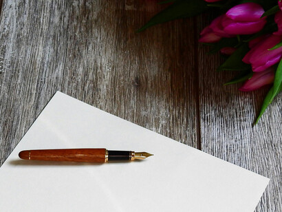 Una mesa con pluma, papel y unas flores