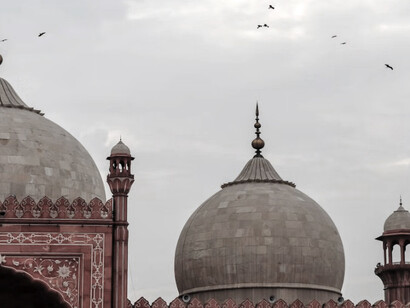 Birds soar over the brown and white domes of Badshahi Masjid in Lahore, Pakistan, on a clear daytime sky