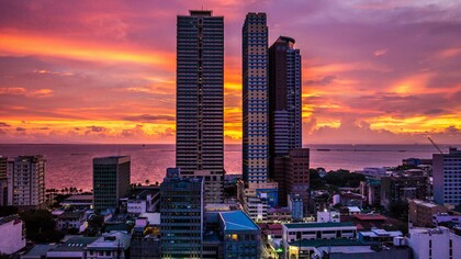 Towering buildings overlooking Manila Bay at dusk, symbolising a city that remains open to history, hope, and endless becoming