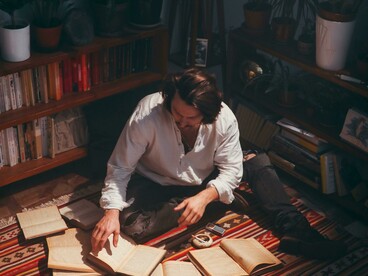 A vintage scene of a man seated on a red carpet, absorbed in poetry