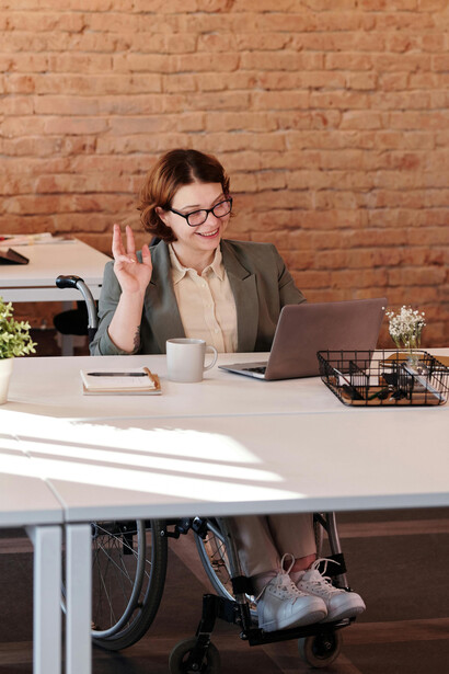 A woman smiling while using a laptop, seated in a wheelchair, embracing technology with confidence despite her disability