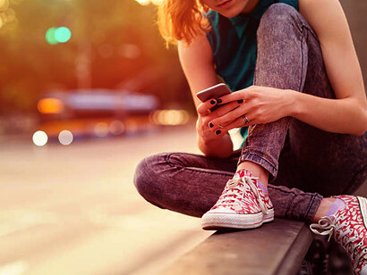 A young woman sitting on the pavement, scrolling through her social media feed