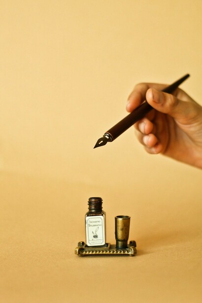 A hand grips a pen, poised to write on the surface of ink bottle