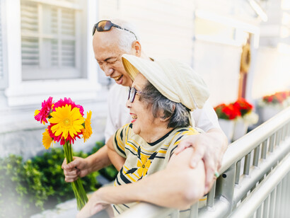 The older husband gives his wife a bouquet of colored daisies near the water