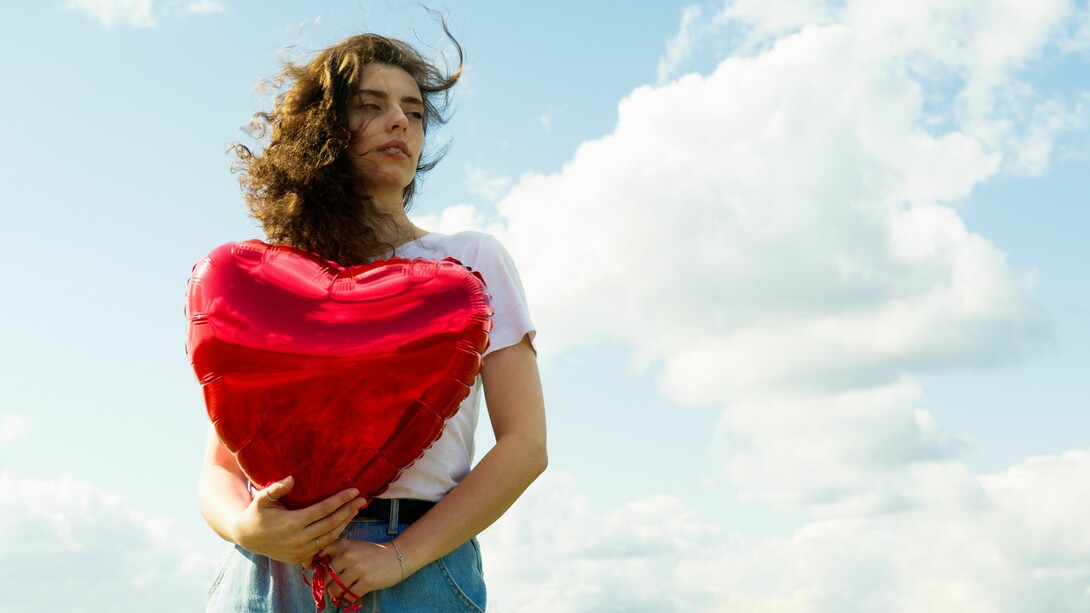 A woman holding a heart-shaped balloon beneath an open sky, representing the ability to protect one's heart without closing it off