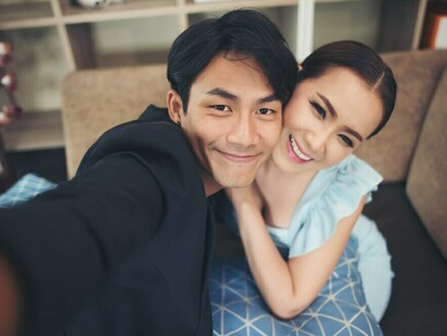 A loving Korean couple sharing laughter while taking a selfie on their cozy couch, embracing happiness and togetherness