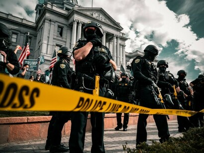 A man in a black police uniform observes a daytime protest, highlighting the escalating conflict between authority and dissent in contemporary society