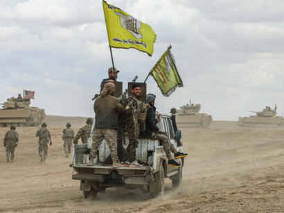 A group of Kurdish fighters gathers near the ruins of a former ISIS stronghold, symbolising both their hard-won victories and the fragile nature of their semi-autonomous control