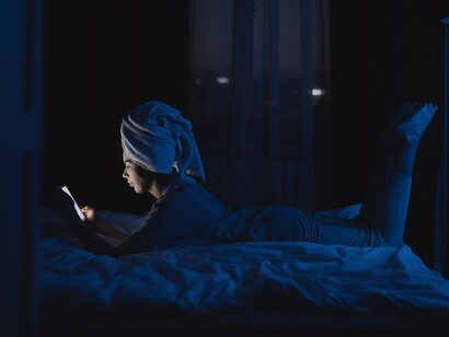 A woman lying on a bed whilst looking at a mobile phone in a dark room