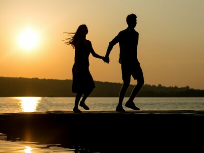 Two figures standing hand in hand beside the river, representing love lasting throughout the passage of time