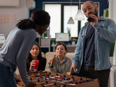 A multicultural team unwinding after work, playing foosball, sharing drinks, and enjoying snacks, highlighting the evolving workplace culture