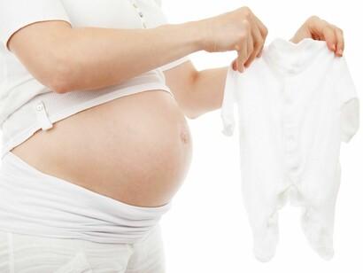 Una embarazada contempla la ropa de su nuevo bebé