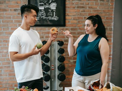 A trainer holding a donught in one hand and and an apple in another to his client