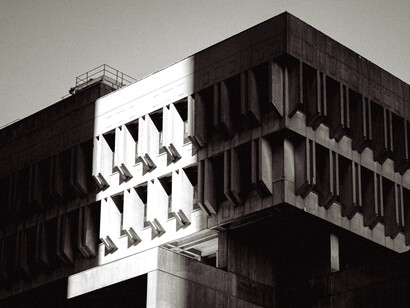 Fotografía en blanco y negro de estilo arquitectónico brutalista, destacando el contraste de una franja de luz vertical que ilumina parte de la fachada de hormigón