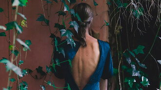 A woman in a blue dress, viewed from behind, standing near an old building
