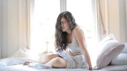 Ragazza siede sul letto dolorante con lo stomaco che le brucia