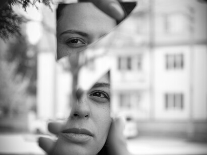 O reflexo de um rosto surge entre o espelho e a fachada de um edifício, criando uma composição de fragmentos, linhas e perspectivas. A identidade individual também se constrói na relação com o ambiente social e com as imagens que aprendemos a reconhecer como verdadeiras