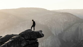 A man standing at the top of a rock mountain seemingly reflecting on life