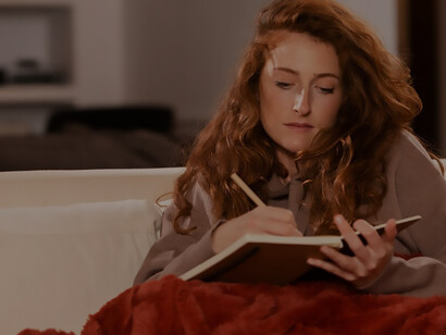 Captured in the warmth of winter, a woman in cozy attire sits on a couch, penning thoughts in serene solitude