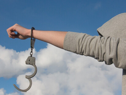 In the powerful visual, the bound hands of a woman break free from handcuffs, reaching towards the vast expanse of the open sky, portraying a profound sense of liberation and determination to overcome limitations