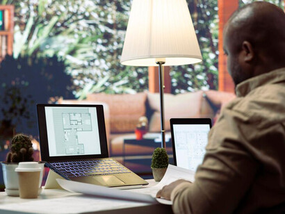 A modern architect's office featuring a computer screen displaying 3D rendering software of a building complex, as a man works on creating a digital twin model