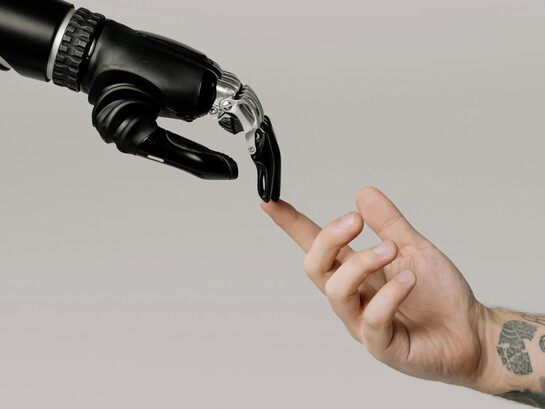 A human and a robotic hand barely touching, alluding to the Renaissance painting "The Creation of Adam", by Michelangelo Buonarroti