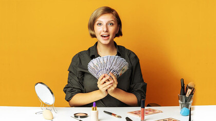 With a confident smile, the woman elegantly showcases a bunch of money in her hand, effectively promoting a line of exquisite makeup products, enticing viewers with both the allure of beauty and financial success