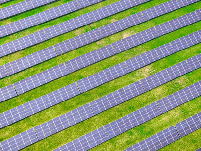 Bird's-eye view of a German landscape with a vast grass field and blue solar panels, showcasing the harmony between agriculture and renewable energy