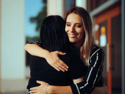 A woman embraces a friend, unaware of the betrayal hidden behind a fake smile