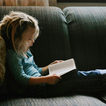 Niño leyendo sentado en un sillón. Los chicos que leen por sí mismos aprenden fuera del código escolar y el contexto cultural propio