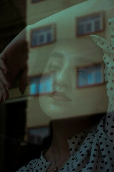 A woman wearing a blue and white polka dot shirt looks out the window, her expression revealing the tension between emotion and reality