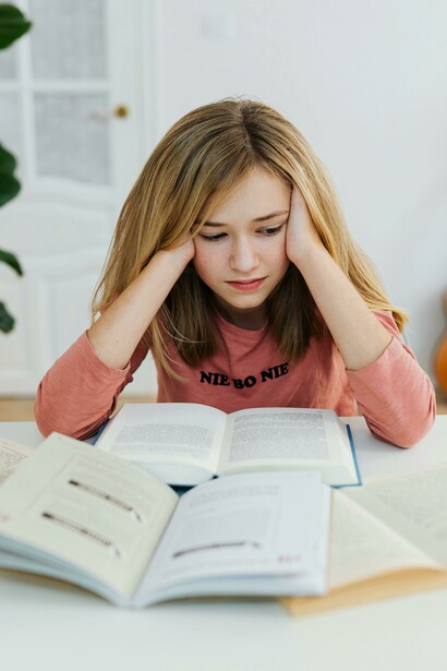 A girl with her head in her hands, bored yet still trying to read as meaning slips away