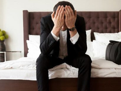 A man, stressed and in pain, sits on his bed trying to cope with his hardships