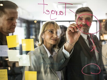 A group of professionals engaged in a strategy session, using sticky notes and a glass board to map out ideas and goals, a visual that reflects the core Agile principles of collaboration, adaptability, and iterative planning